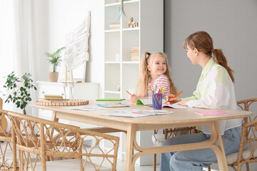 Nanny with cute little girl drawing on table at home