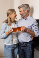 Joyful senior couple drinking tea together at kitchen table enjoying morning conversation