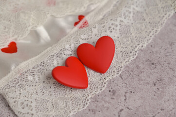 Couple of red earrings heart shape on lace. Gray concrete background. White cloth with heart shape pattern. Preparation to Valentine's Day. Female look of the day