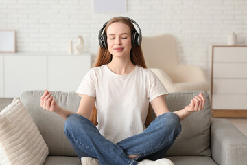 Obraz premium Young pretty woman in headphones meditating and listening music on sofa in living room