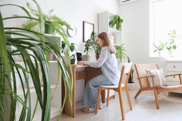 Young woman working with laptop and plants at table in office
