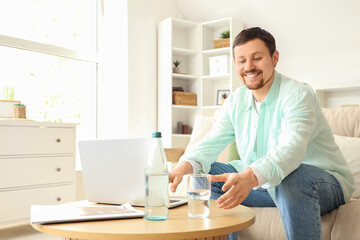 Obraz premium Young man with laptop taking glass of water from table at home