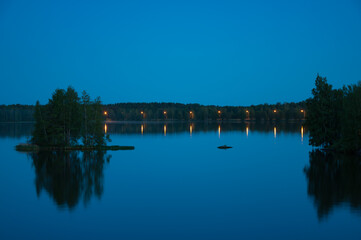 Obraz premium Early summer night by a calm lake in Finland with street lights lining the shore