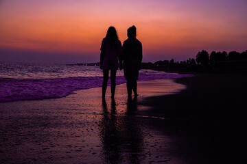 Photo of two girls holding hands at sunset by the sea