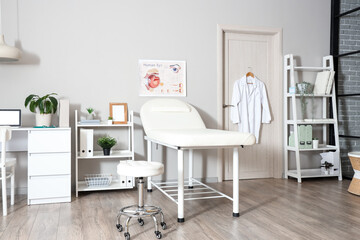 Interior of light medical office with couch, shelf units and doctor's workplace