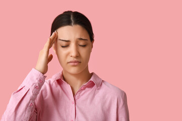 Beautiful young woman suffering from headache on pink background