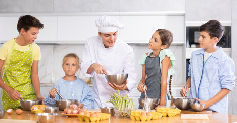Cooking class, culinary, food and people concept - happy group of children and male chef cook cooking in kitchen