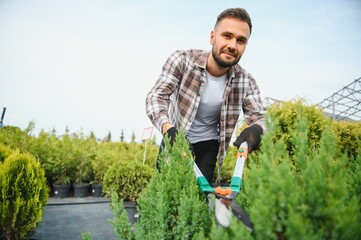 A young gardener cuts a tree with scissors. Gardening and tree shop concept