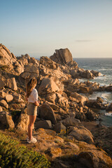 Woman admiring sunset over capo testa granite coastline in gallura, north sardinia, italy