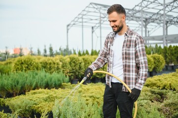 Young male gardener watering plants with a shower head and hose