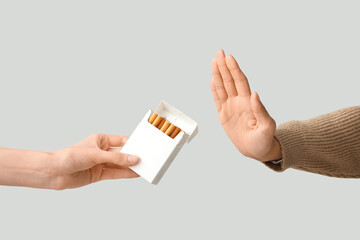 Female hand rejecting pack of cigarettes on grey background. Stop smoking concept