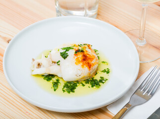 Roasted sepia served with piquant green sauce on white plate..