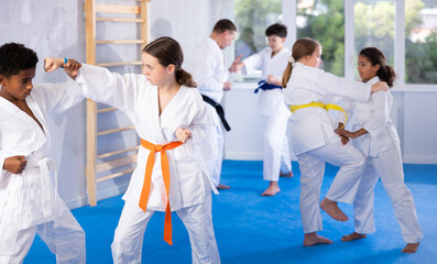 Concentrated teenage girl in kimono practicing punches during training sparring with african...