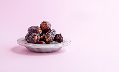 Sweet,dried date fruits in stylish pink glass bowl on pink bankground with large copy space