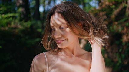 Naklejka premium Smiling woman warming sunlight in park looking camera. Girl touching hairstyle