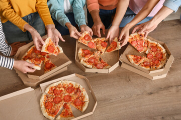 Group of friends taking pepperoni pizza from table in kitchen