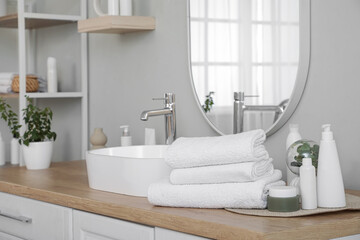 Stack of clean towels and cosmetic products on table in bathroom