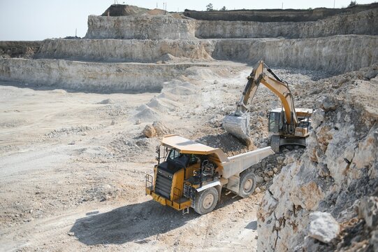 Heavy mining truck and excavator, close-up, against the background of the panorama of a limestone quarry