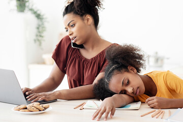 Bored african american teen girl sitting by her working mom, busy black lady having phone...