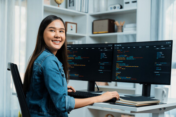Young Asian in IT developer looking at camera to present with online information on pc with coding program data application, wearing jeans shirt. surround by safety analysis two screens. Stratagem.