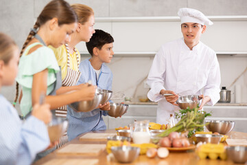 Young guy chef at master class teaches group of children how to cook food
