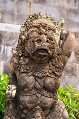 Close-up of a timeworn Balinese statue, revealing detailed carvings and a sense of antiquity. Lush greenery frames the sculpture, highlighting its cultural artistry.