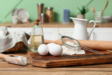 Cutting board with fresh eggs, flour, oil and utensils for preparing dough on wooden table in kitchen