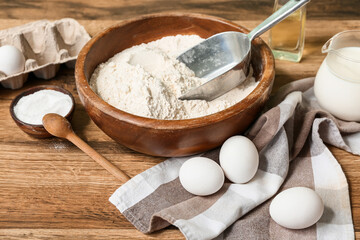 Fresh eggs, bowl of flour, oil, baking soda and milk on wooden table