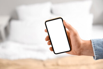 Young man holding blank mobile phone in bedroom, closeup