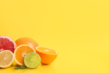Different cut citrus fruits and mint leaves on yellow background