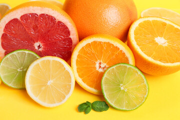 Different cut citrus fruits and mint leaves on yellow background