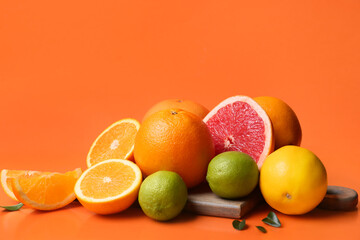 Wooden board with different cut citrus fruits and leaves on orange background