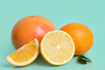Different cut citrus fruits and leaves on turquoise background