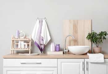 Cosmetic products and clean towels hanging on grey wall near modern sink in bathroom