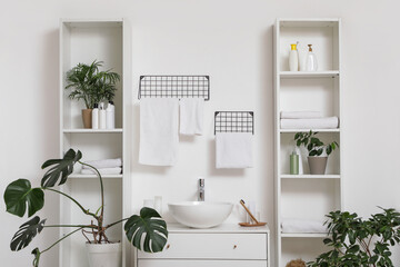 Houseplants, cosmetic products and clean towels on shelving units near modern sink in bathroom