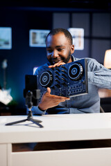 Artist filming DJ mixing tutorial in recording studio, pressing different buttons to show device...