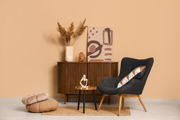 Interior of living room with armchair, coffee table and home decor on commode near brown wall