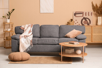 Interior of living room with grey sofa, coffee table and home decor in shelving unit near brown wall
