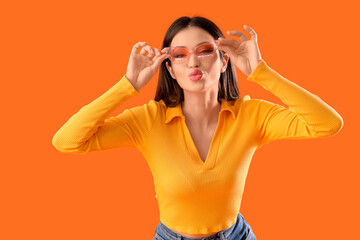 Young woman in sunglasses blowing kiss on orange background