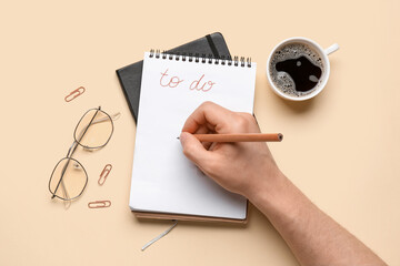 Male hand with to-do list, cup of coffee and eyeglasses on yellow background