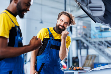 Repairmen in auto repair shop working together on fixing car, excited after finally finding issue. Jubilant colleagues glad to be able to repair broken vehicle after many efforts
