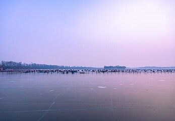 Crowds gather on frozen lake for winter festivities at sunset with colorful sky