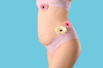 Young pregnant woman in panties with gerbera flowers on blue background, closeup