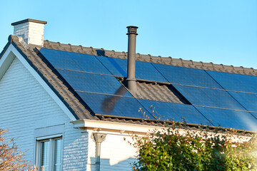 Fototapeta premium House with solar panels. Photovoltaic panels on the roof. Sun rays and greenery. 