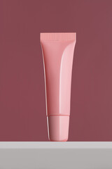 Mockup of a pink plastic tube for cream, lip gloss and other cosmetic grooming products on a pink...