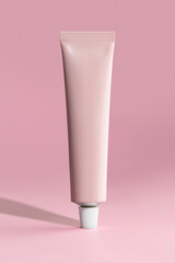Mockup of a pink metal tube for cream, paint and other cosmetic care products on a pink background