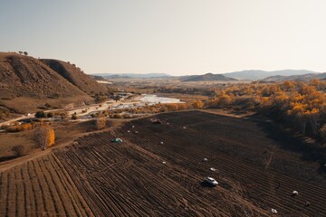 Agricultural field with vehicles and hillside near river during autumn in rural landscape