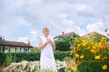 Outdoor portrait of thankful mature woman enjoying summer flowers in cosy garden