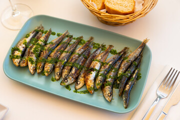 Portion of fried sardines served on plate, flavoured with pesto sauce. Roasted fish on table.