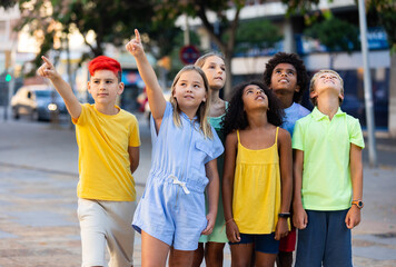 Fototapeta na wymiar Inquisitive carefree tweens spending time outdoors together during summer vacations, looking up at sky and pointing at something ..
